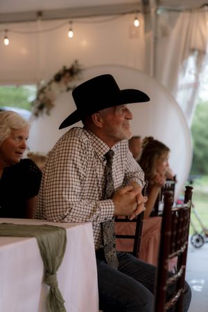 A guest in a black cowboy hat and checkered shirt watches the wedding ceremony.