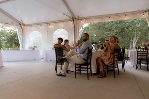 Wedding guests enjoying the reception under a white tent with string lights and outdoor views.