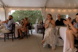 Wedding reception guests seated at tables applauding during celebrations under a tent.