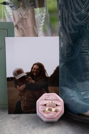 Pink octagonal ring box displayed between cowboy boots and white cards.