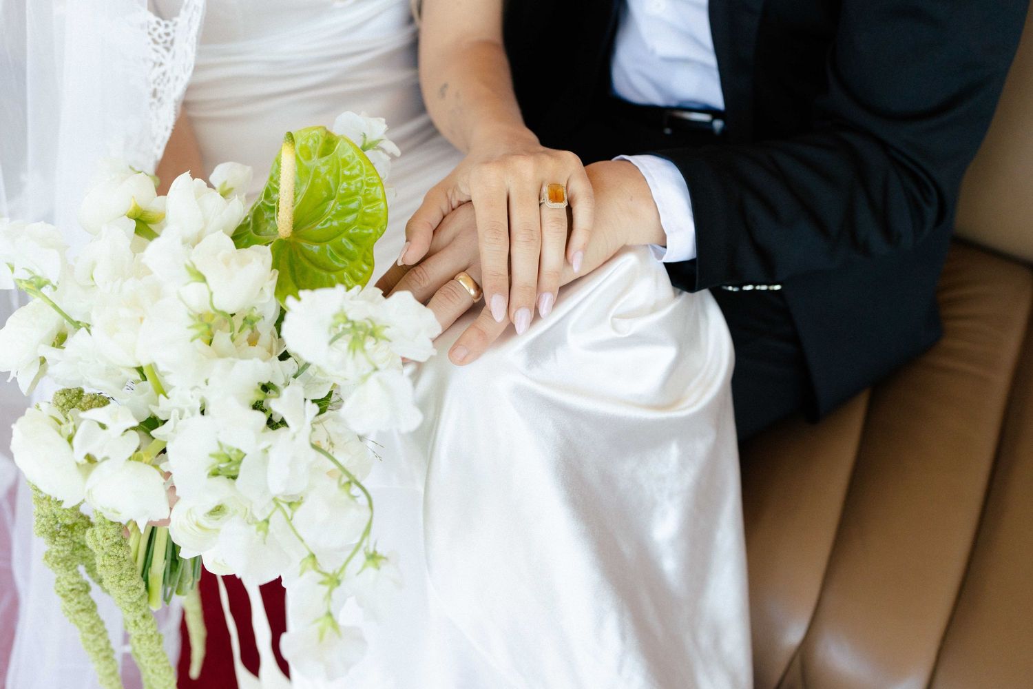 A wedding couple holding elegant white hydrangea and rose bouquets against a light background.