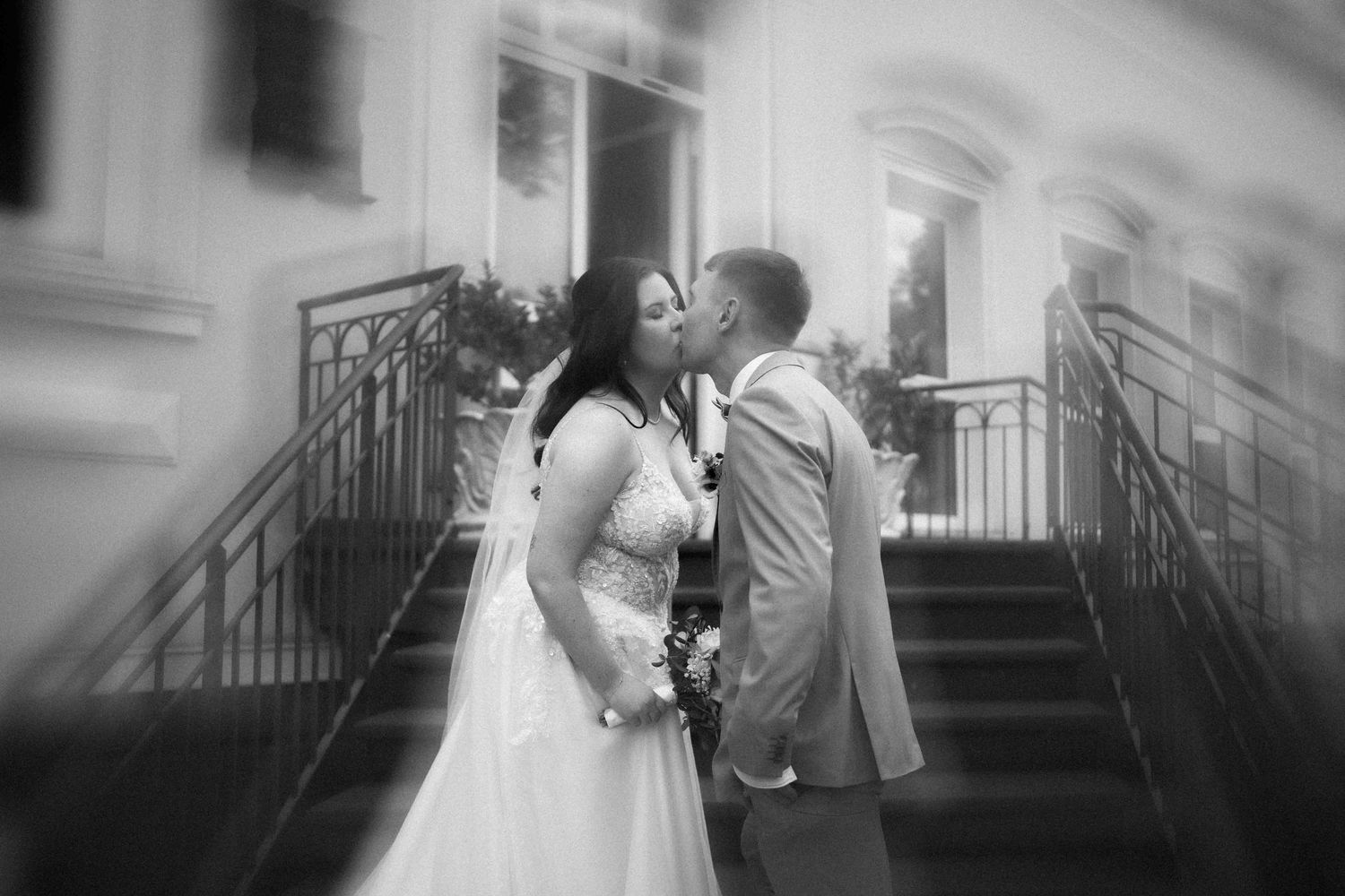 A romantic black and white portrait of a couple on ornate stone steps.