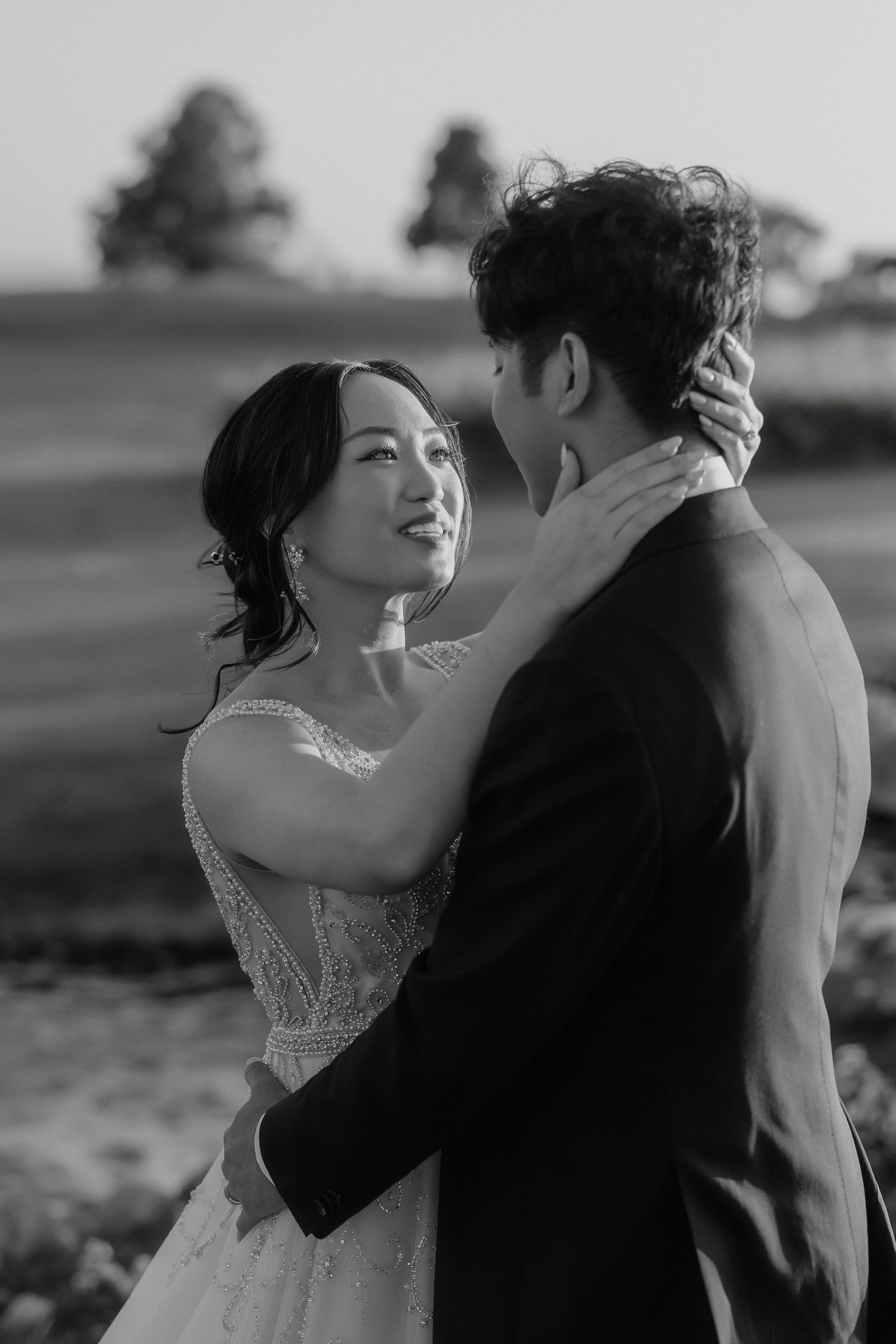 A romantic black and white wedding portrait capturing an intimate moment between a couple outdoors.