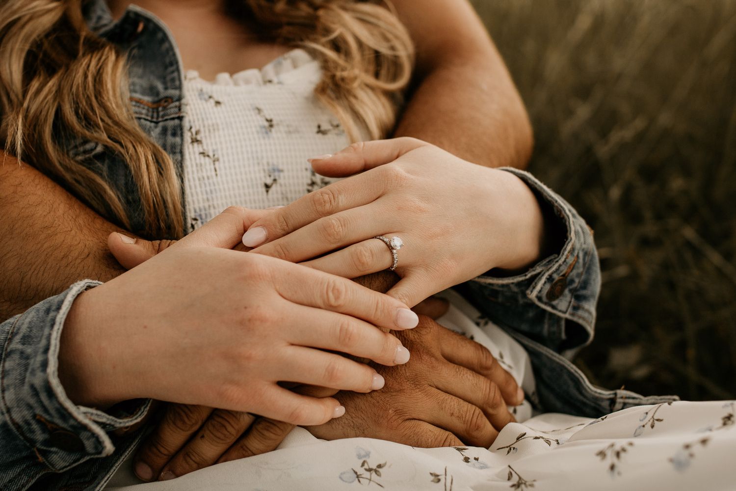 Close-up of hands with an engagement ring resting on floral fabric during a romantic photoshoot.