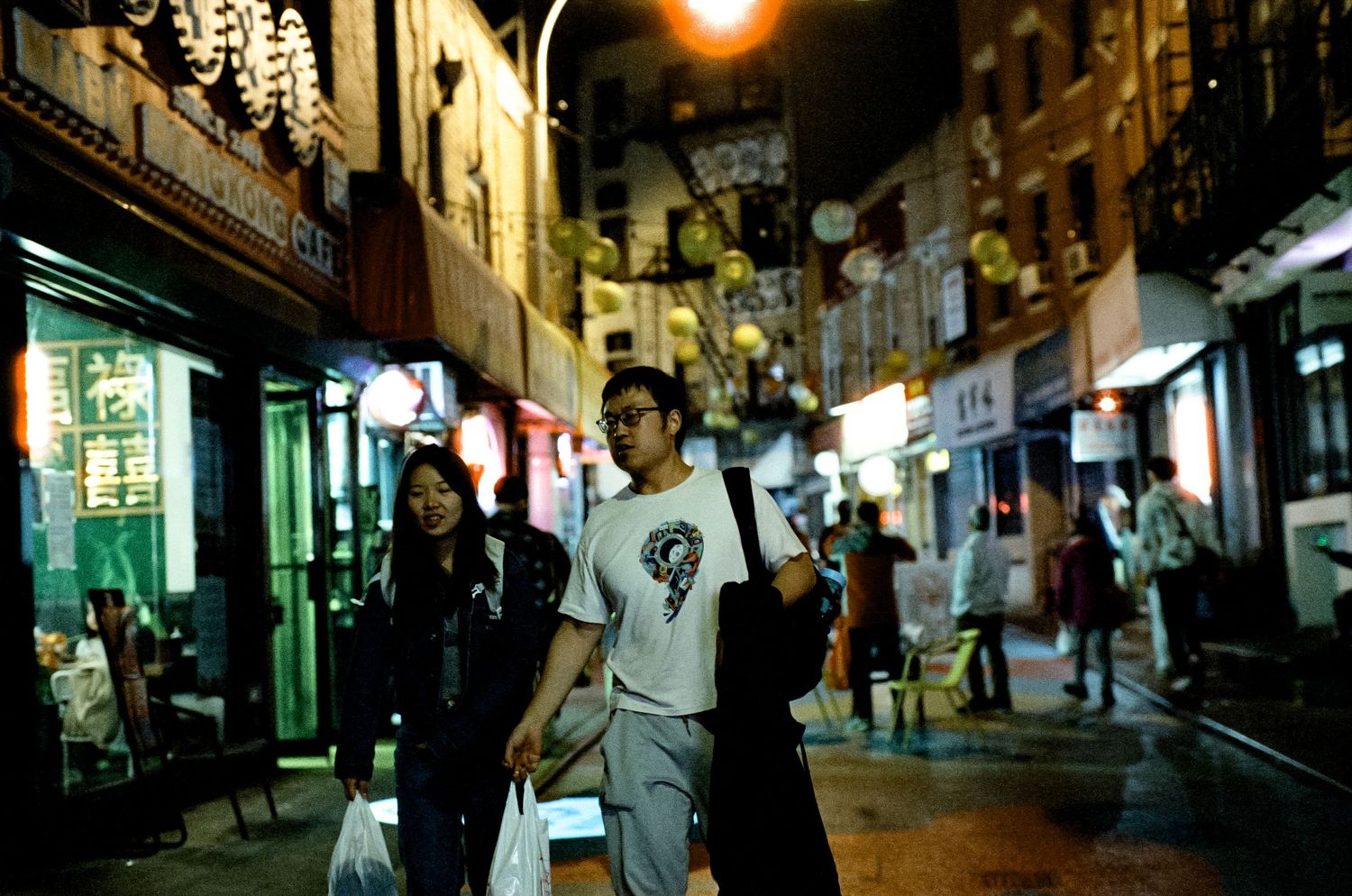 Bustling nighttime street in Japan with lanterns and shops illuminated by warm lighting.