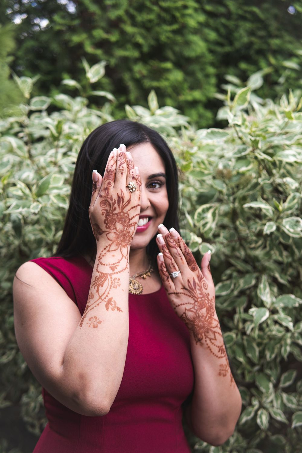 Close-up of intricate henna designs on hands against a leafy background.