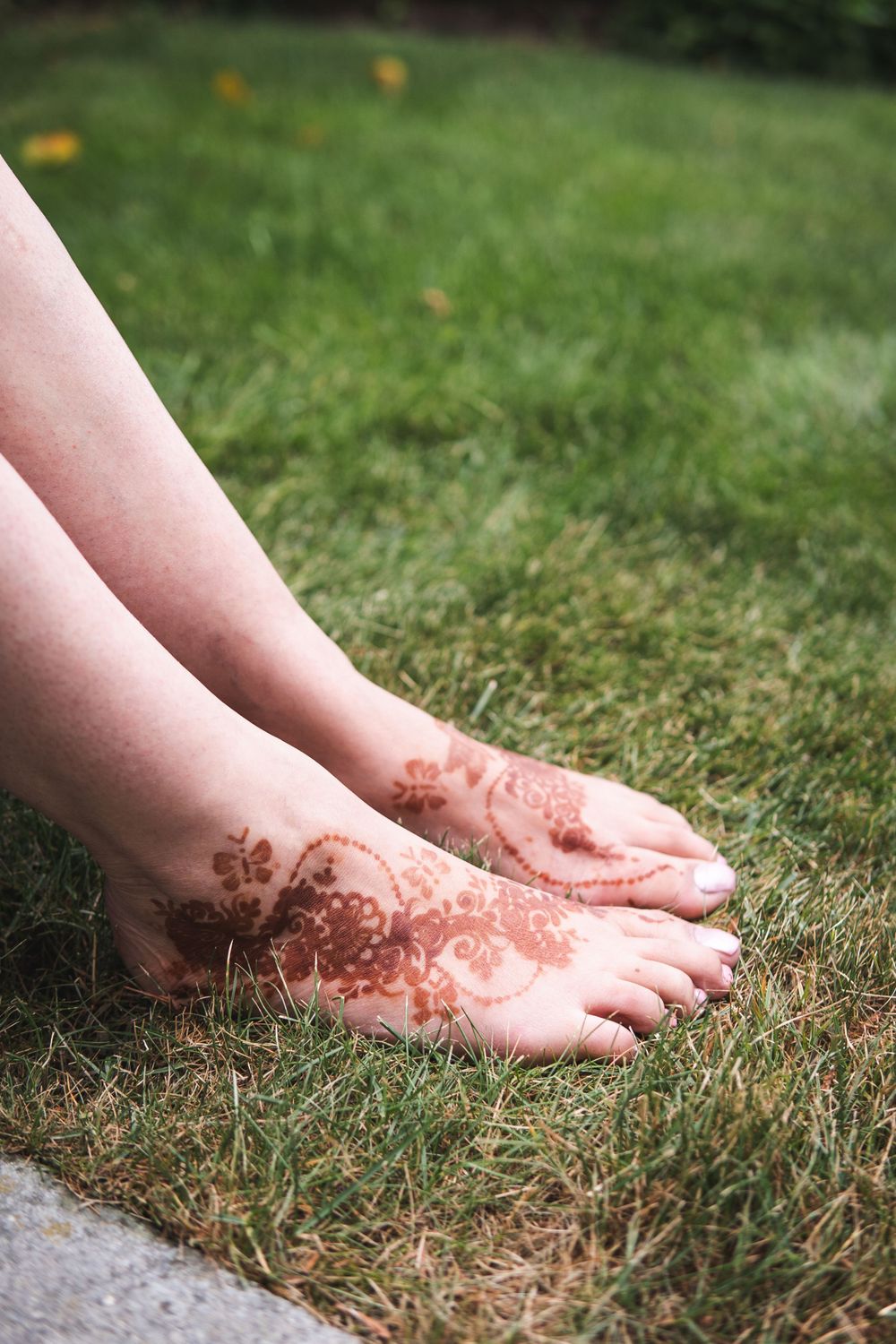 Delicate henna designs adorning bare feet on green grass.