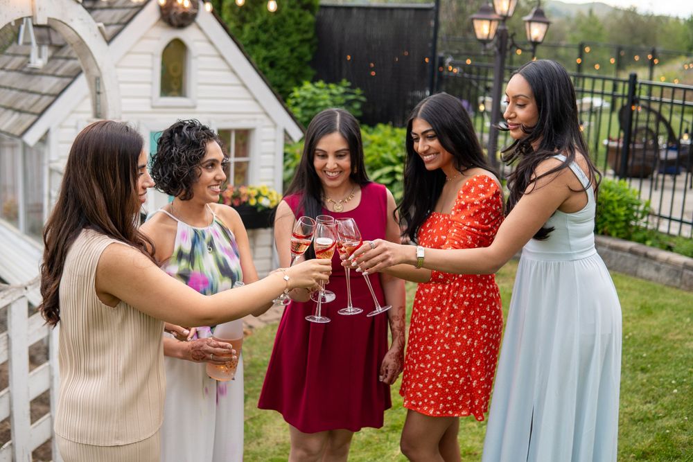 Friends in elegant dresses toasting with drinks at an outdoor celebration.