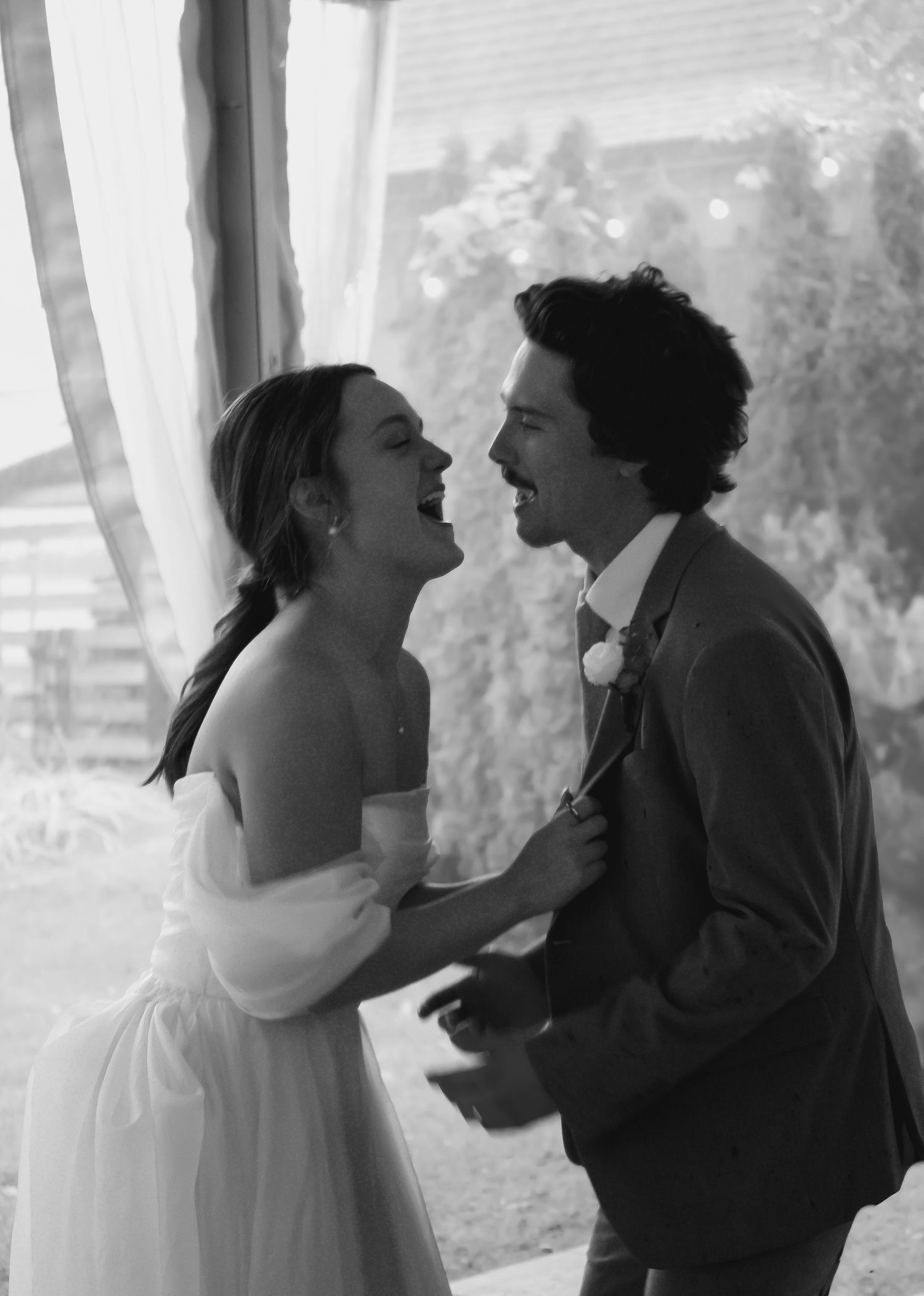 A tender black and white wedding moment captured between a couple near a window.