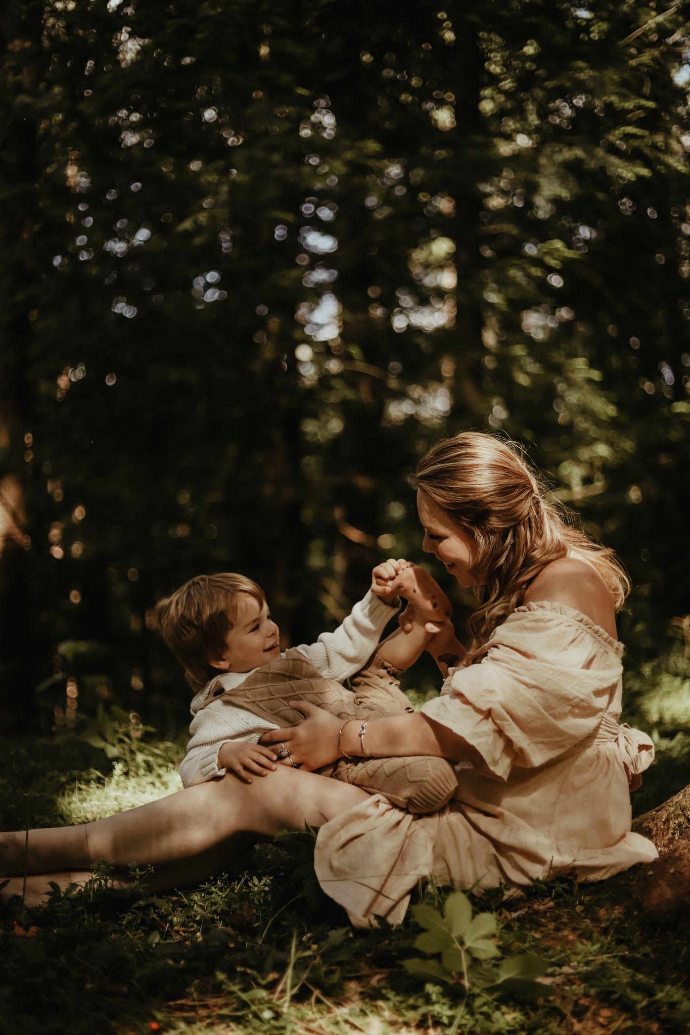 A tender moment between mother and child lying in dappled sunlight on forest ground.