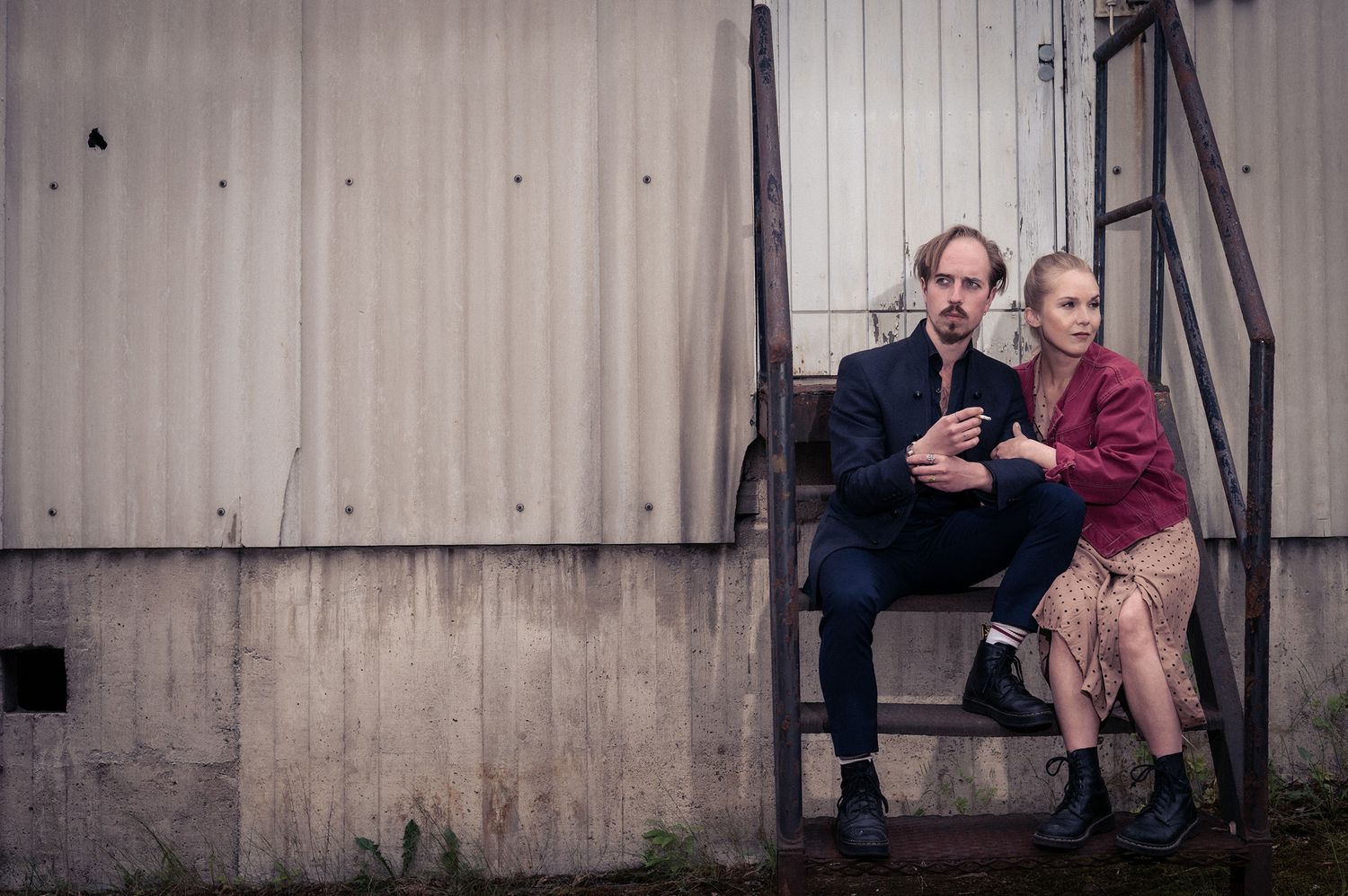 Pariskunta istuvat rappusilla kihlajaiskuvassa, teollisuusalueella Turussa.