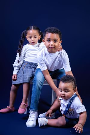 Three siblings pose together against a dark blue studio background.