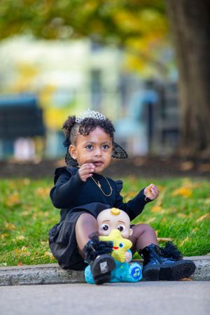 A toddler plays with Minion toy while wearing navy dress and tiara outdoors.