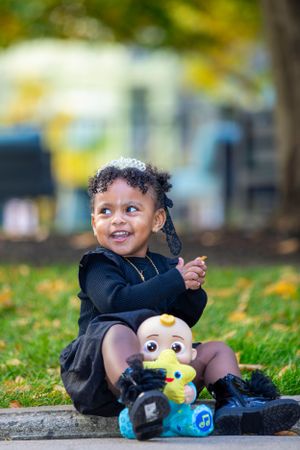 A happy toddler in navy dress poses with Minion toy during autumn photo session.