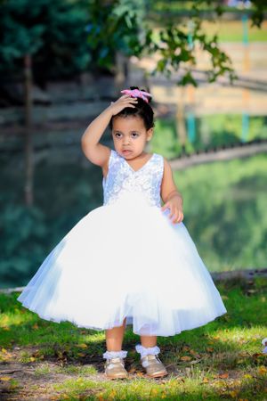 Young child in a white tulle dress and sandals standing outdoors in a garden setting.