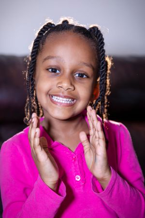 Child in pink sweater smiling with hands raised.