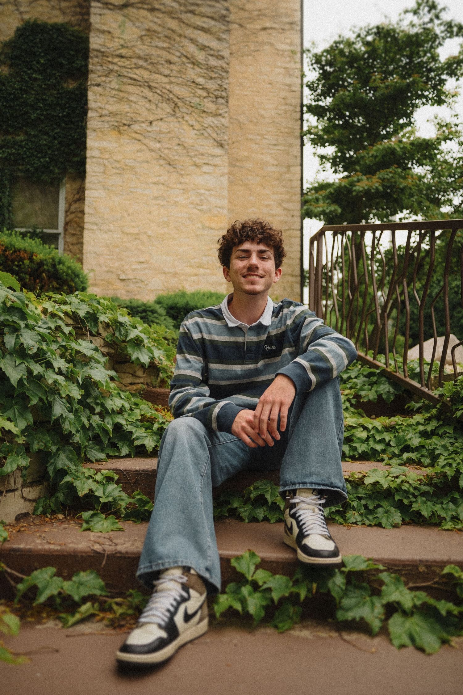 A person in a striped sweater sits casually on outdoor steps surrounded by ivy and stone columns.