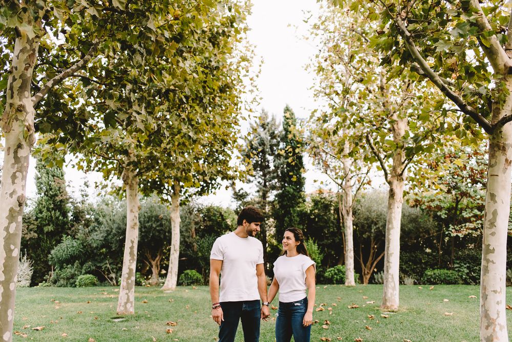 Couple holding hands while walking through a tree-lined park path on a sunny day.