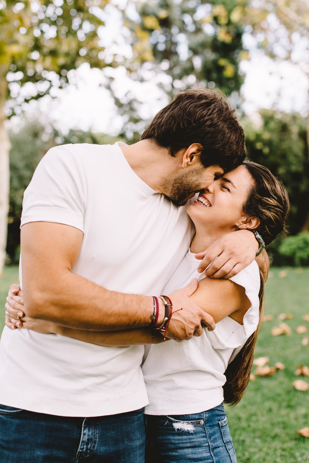 Happy couple in white t-shirts embracing and laughing together in a green park outdoor setting.
