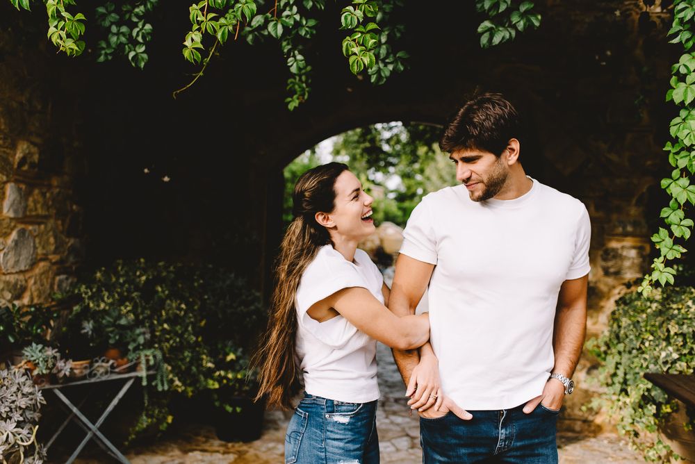 Happy couple in white t-shirts holding hands and laughing together in a lush garden setting.