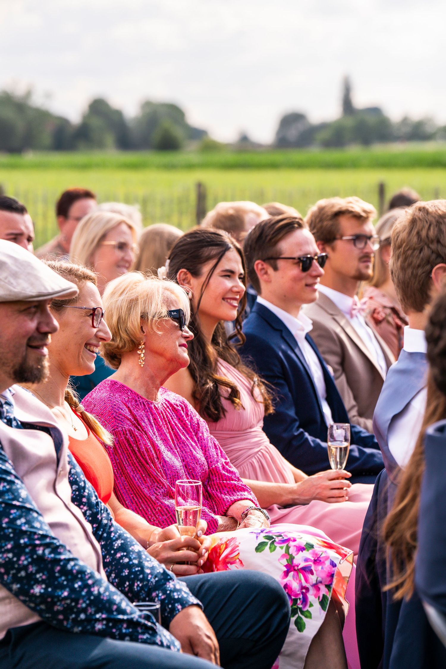 Guests enjoying outdoor celebration with drinks, featuring bright pink attire and sunny atmosphere.