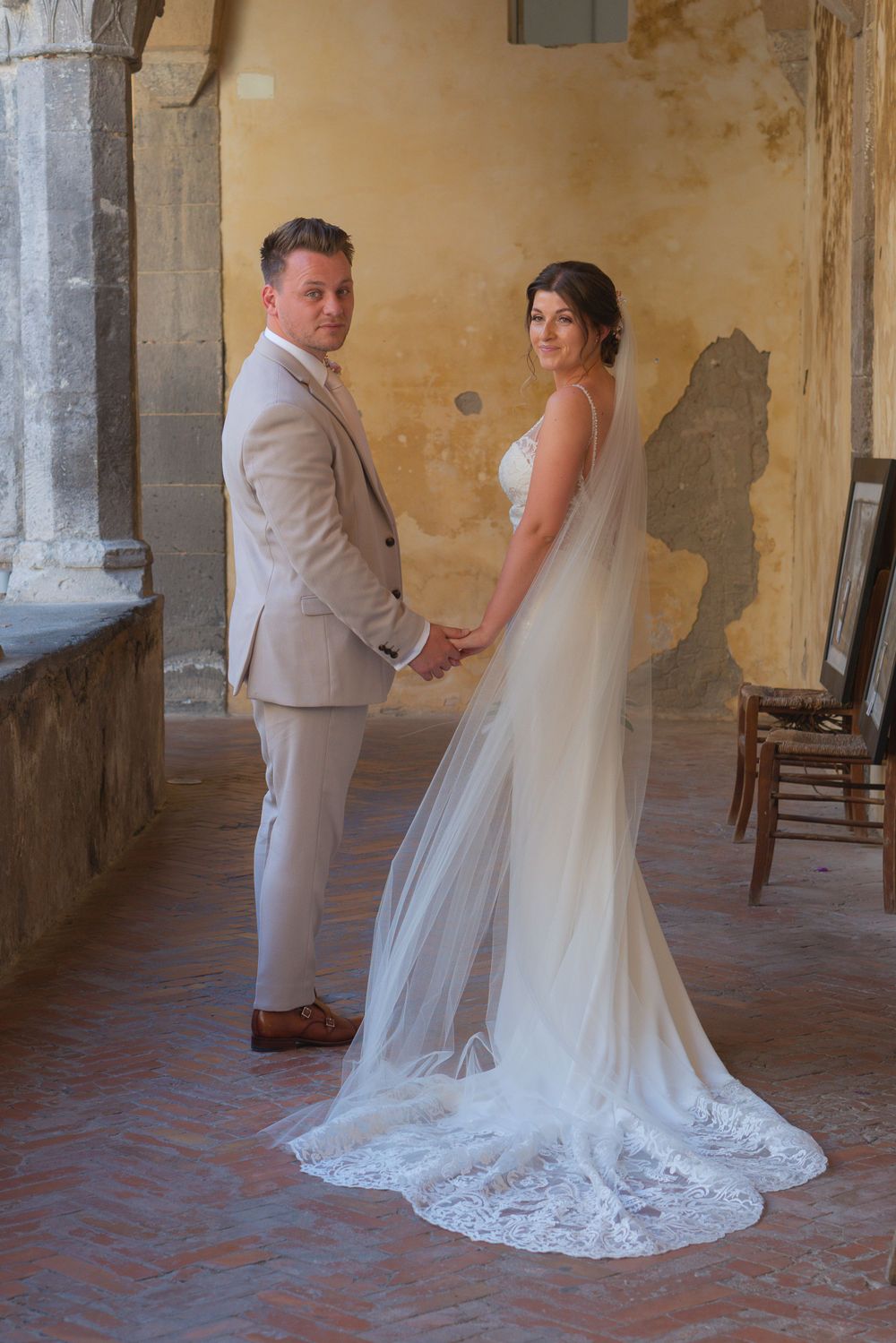 Bride and groom holding hands, walking away from the camera, looking over their shoulders back at the camera.