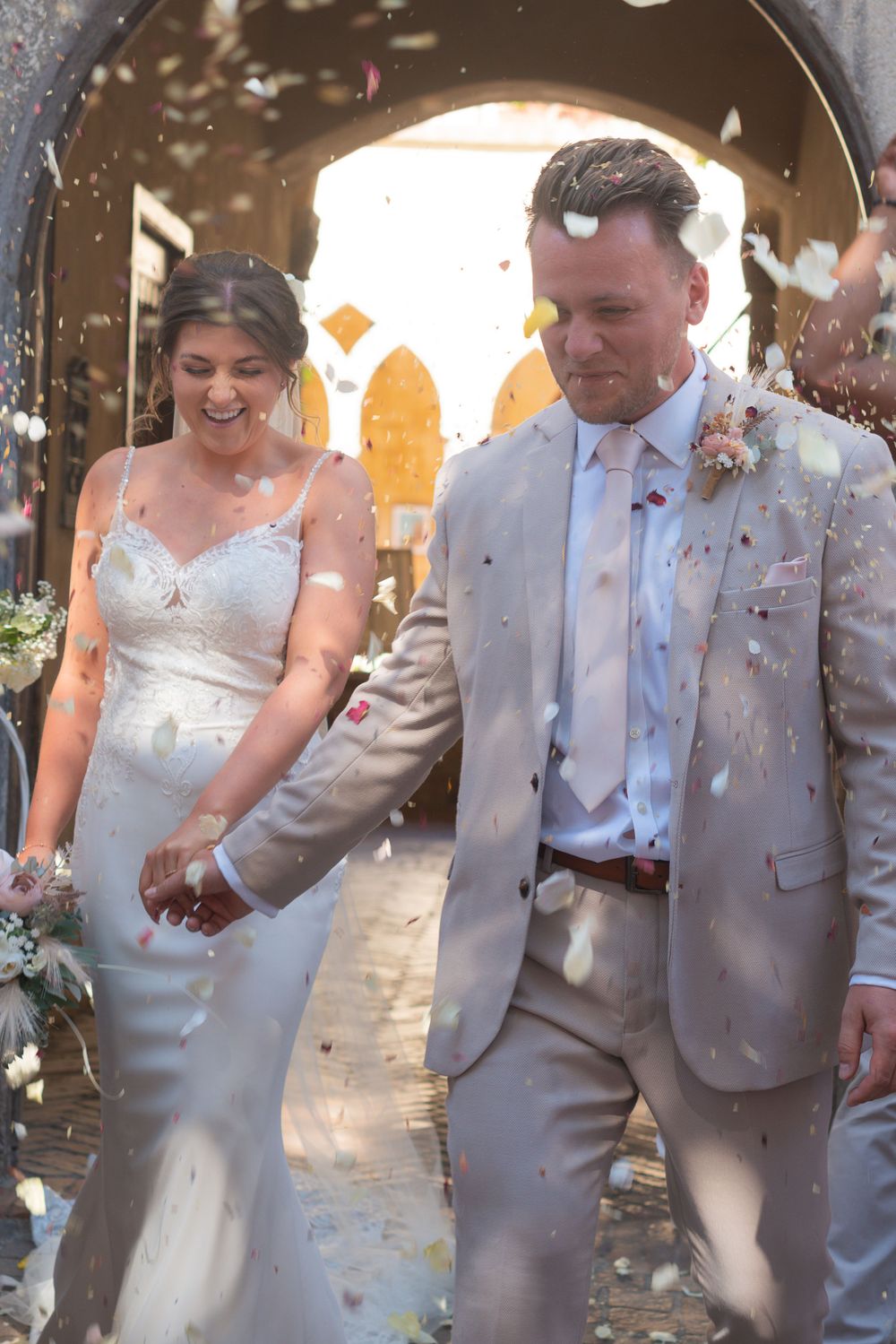 Bride and groom exiting their wedding ceremony, straight in a confetti shot. The bride has a big smile on her face and her eyes shut!