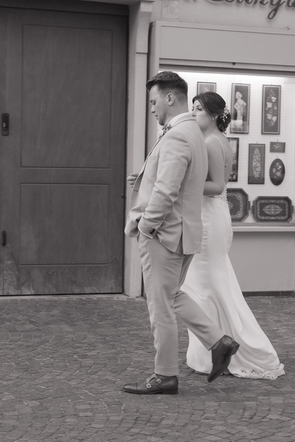 A black and white image of a newlywed couple, casually walking together, arm in arm.