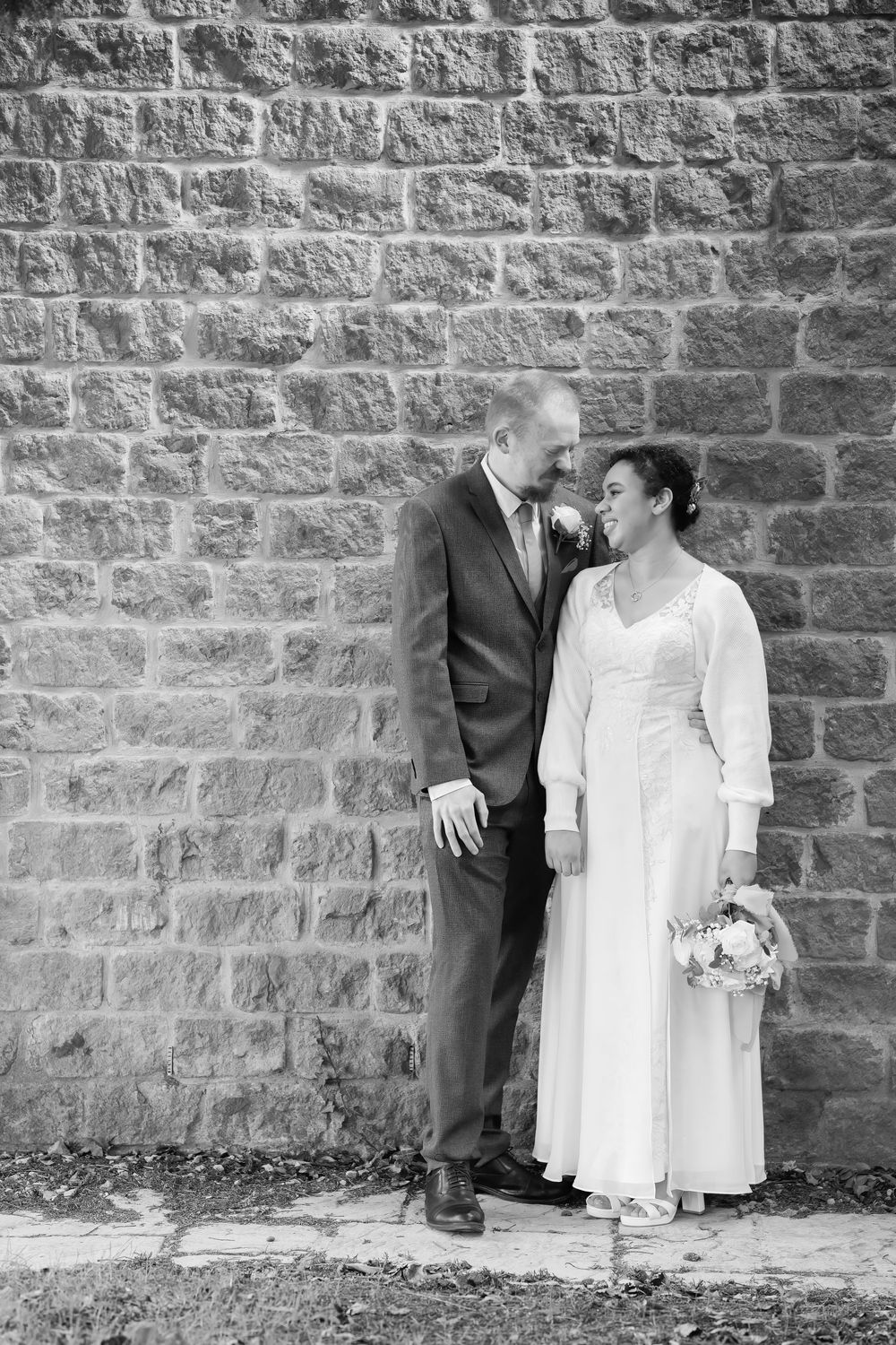 Black and white of a newly married bride and groom, in front of a stone wall.