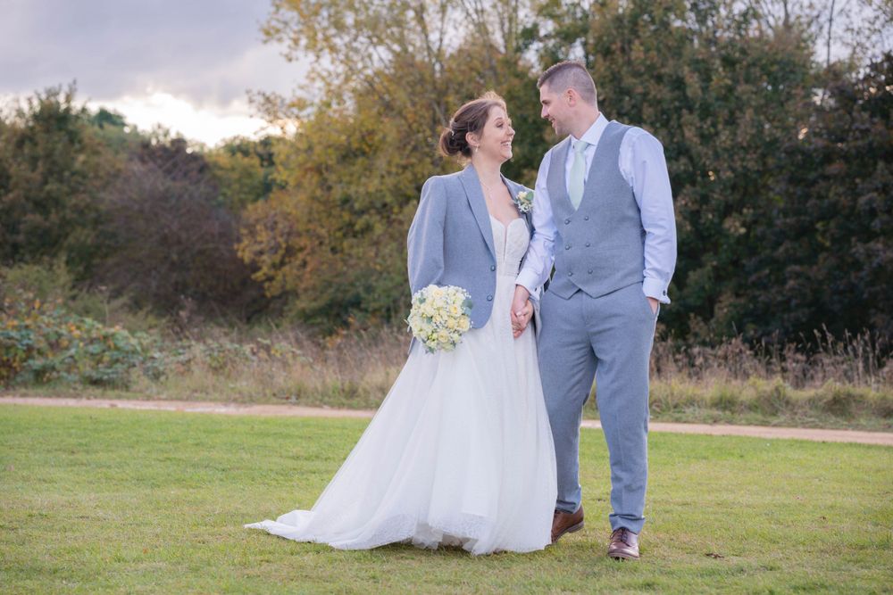 Newlywed bride and groom holding hands, walking towards the camera, gazing at each other. Bride is wearing the grooms jacket to keep warm