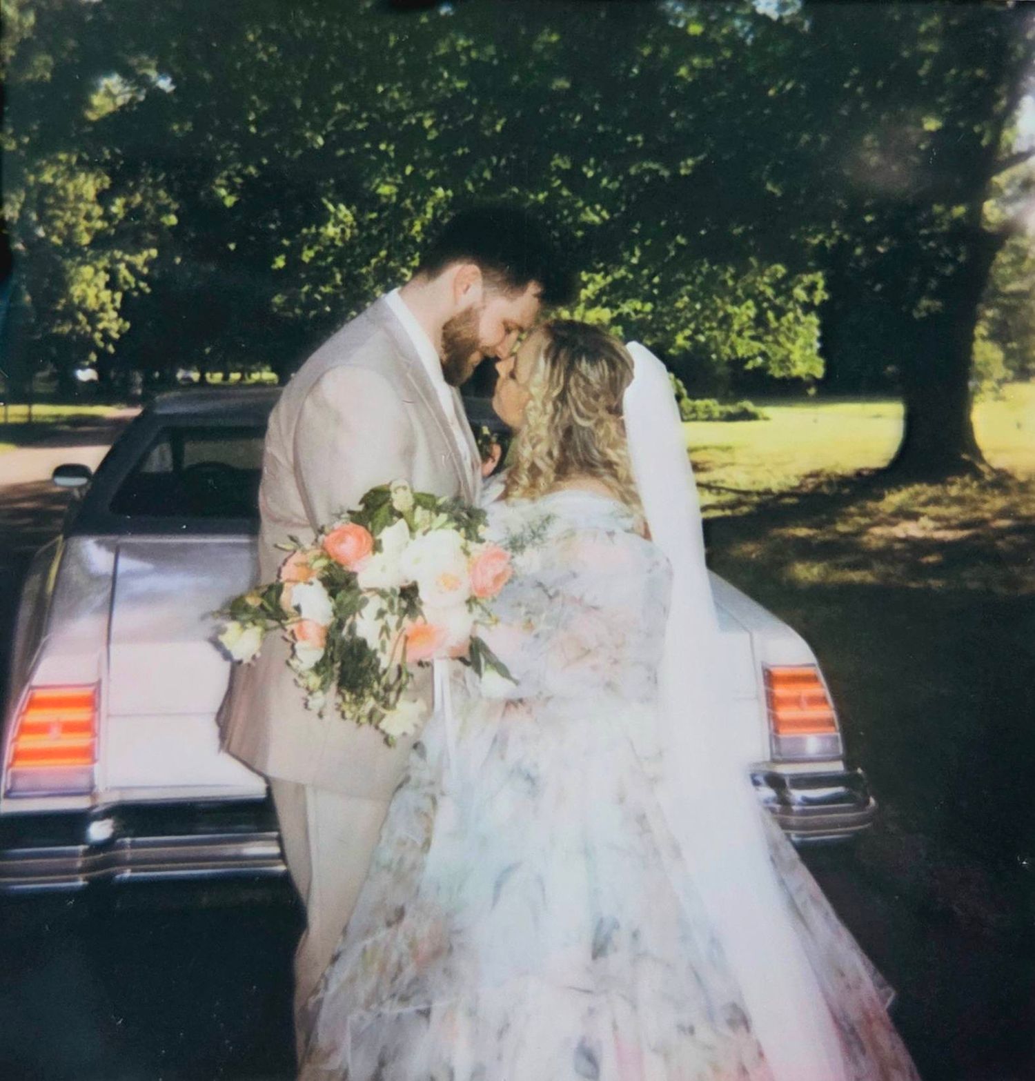 Wedding photo of a couple posing in front of white curtains and floral artwork.