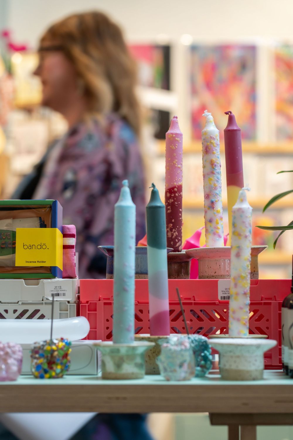 Colorful decorative candles in pastel and floral patterns displayed on a table with craft supplies in the background.