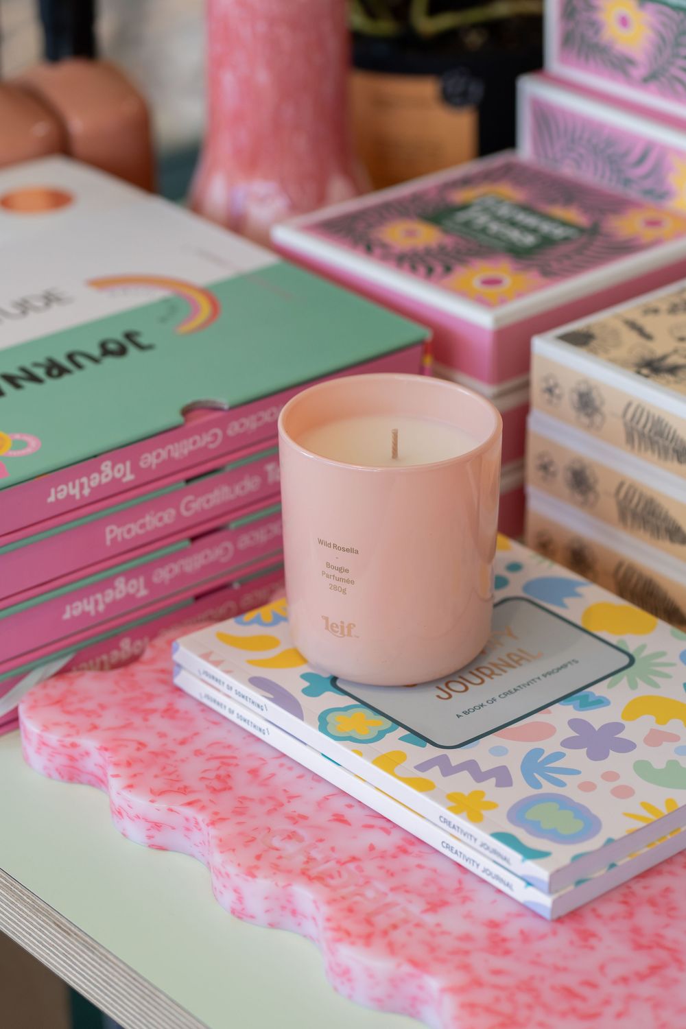 A decorative pink glass jar sits on a floral patterned surface next to books in pastel colors.