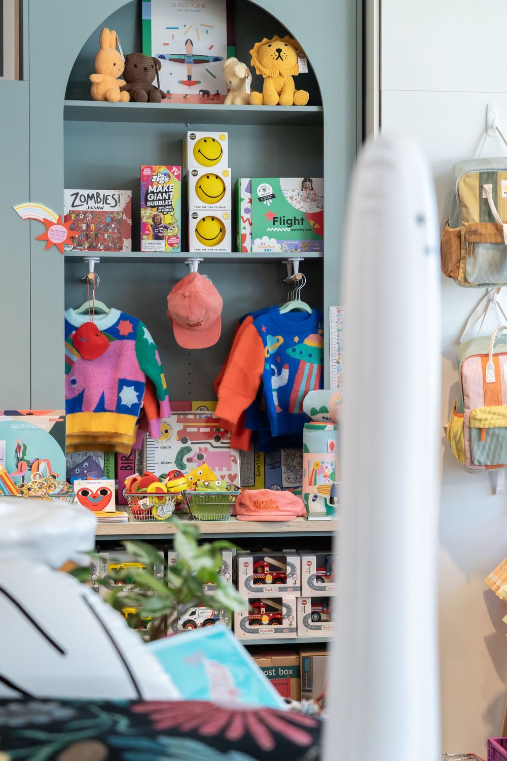 A colorful retail shelf display with stuffed animals, caps, toys and snacks arranged in an arched bookcase.