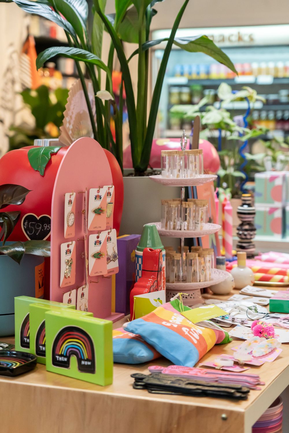 Colorful retail display featuring pink mailbox decor, rainbow cards, and potted plants in a stationery store.