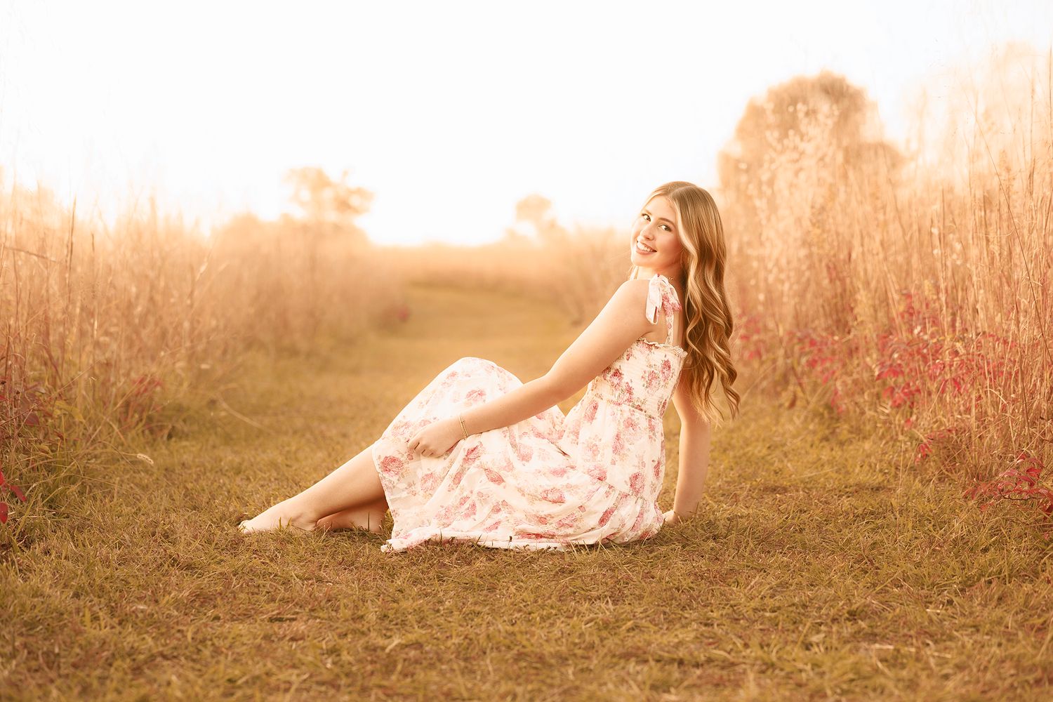 A dreamy portrait of someone in a lace dress sitting in a golden field at sunset.