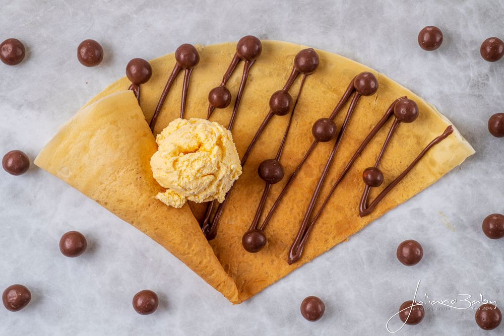 Sweet crepe dessert decorated with chocolate drizzle and whipped cream on gray surface.