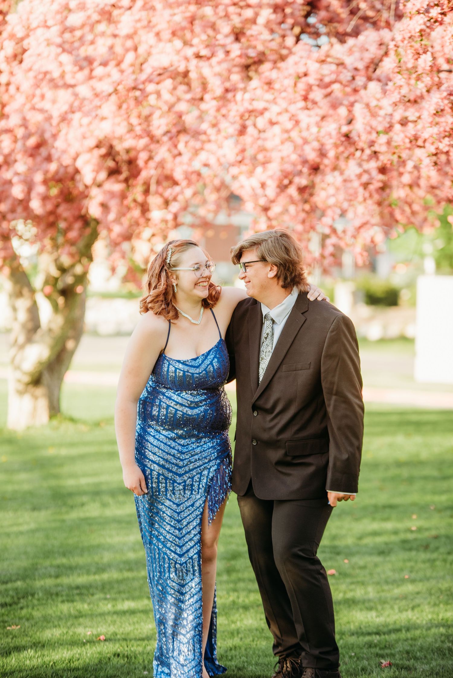 Couple in formal attire sharing a moment under blooming cherry blossom trees.