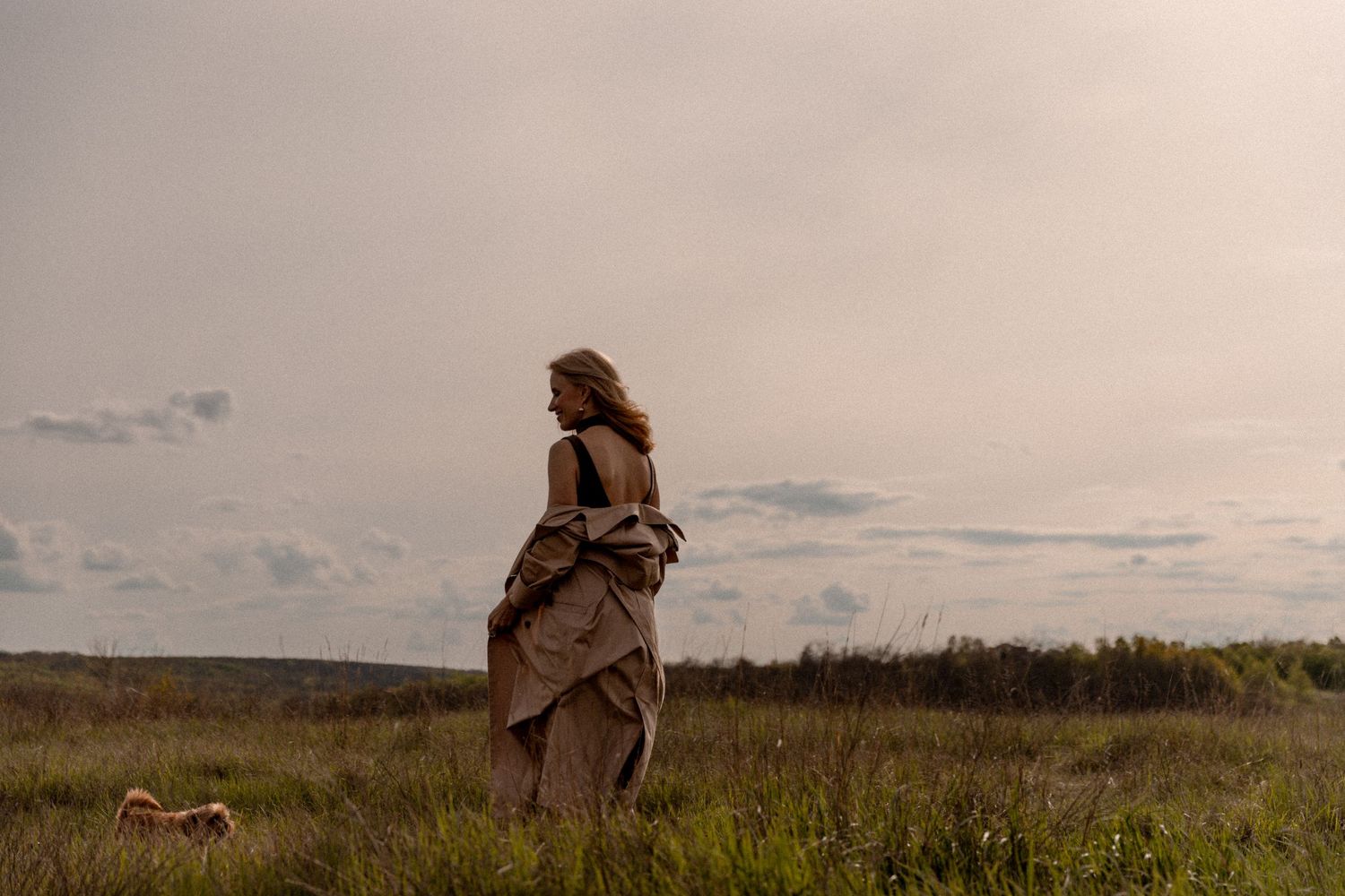 Dreamy silhouette of person in flowing dress standing in windy meadow at dusk.