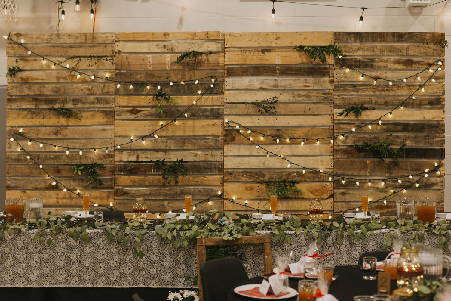 Rustic wooden wall decorated with string lights and greenery creates an ambient wedding reception backdrop.