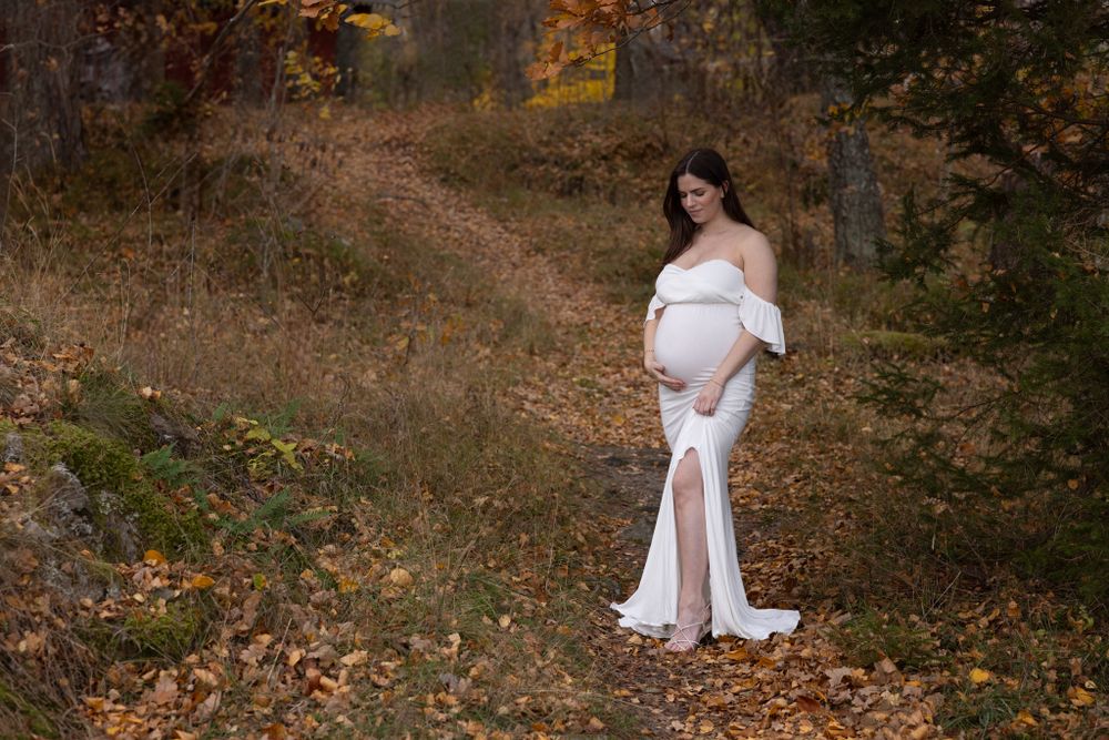 gravid kvinna i vit klänning i höstfärgad bakgrund
