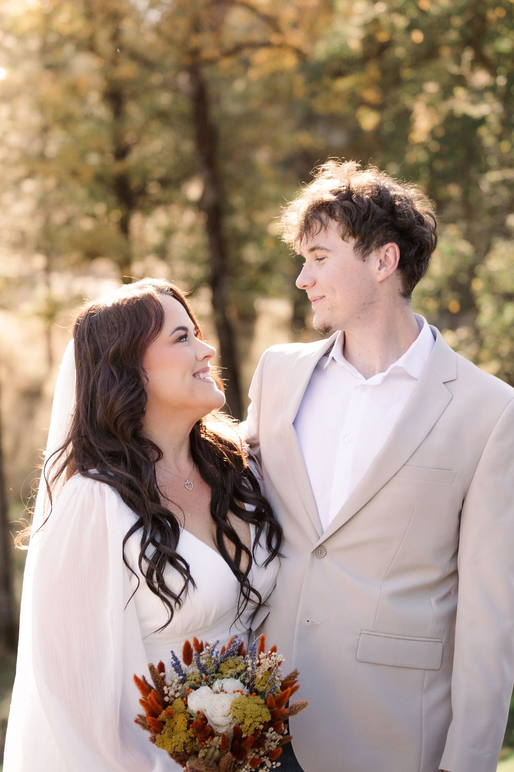 A couple shares romantic moments in an outdoor autumn setting with golden sunlight filtering through trees.