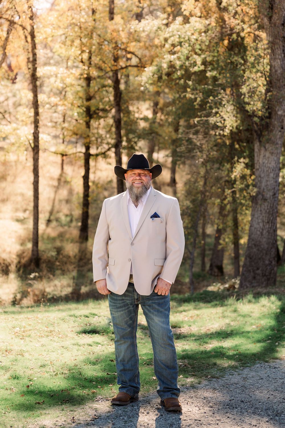 A rustic wedding portrait of groomsmen wearing beige vests and cowboy hats in a wooded setting.