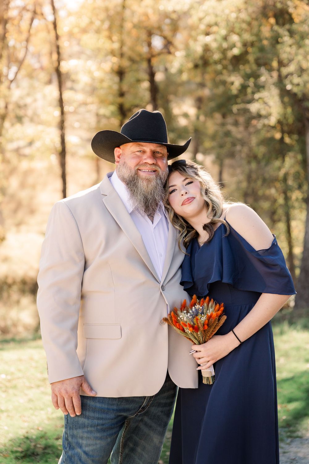 A couple shares a tender moment outdoors while holding dried orange flowers against an autumn backdrop.