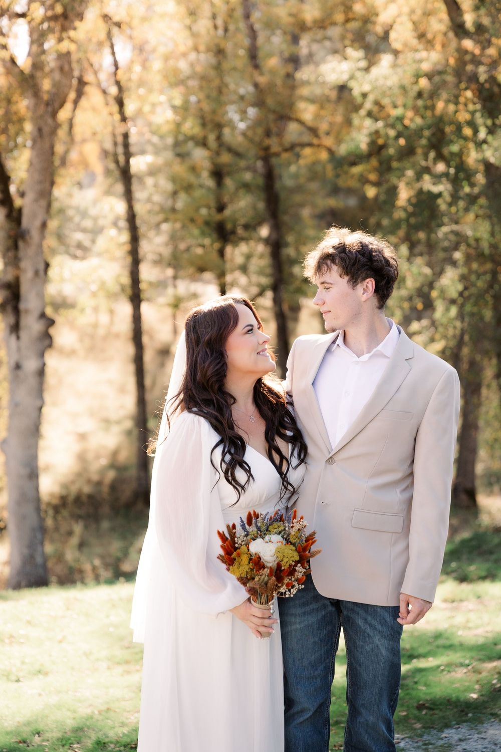 Couple in wedding attire walking together through an autumn forest setting.