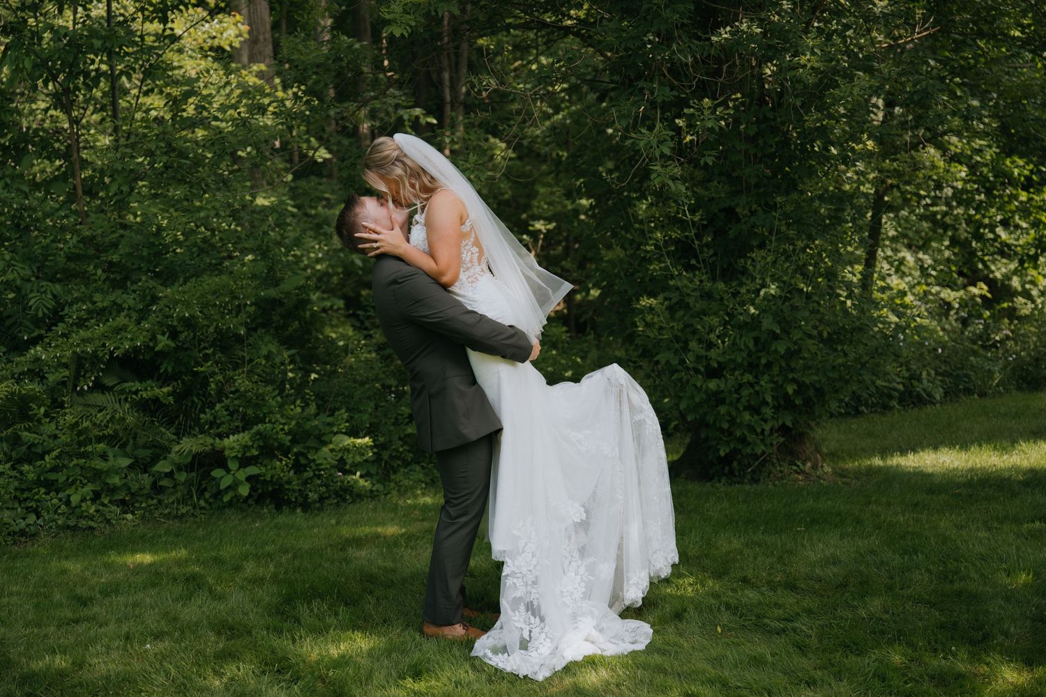 A couple in formal wedding attire embraces and dances together in a lush green garden setting.