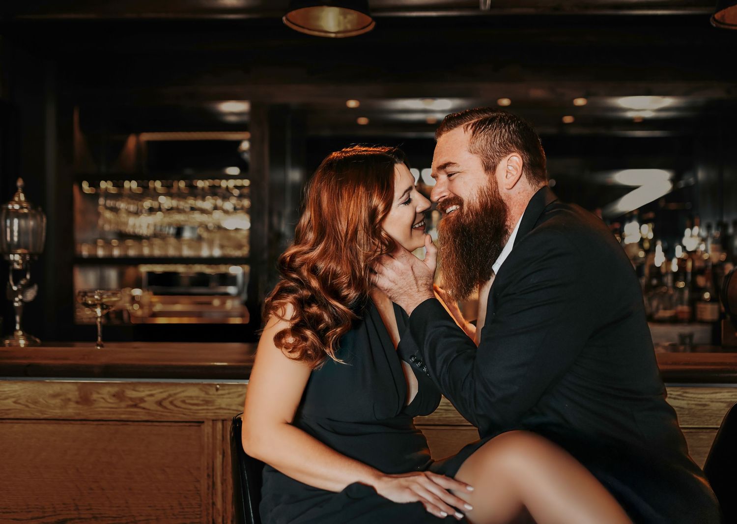 Romantic editorial engagement photo of a couple posing together in an intimate bar setting with moody lighting