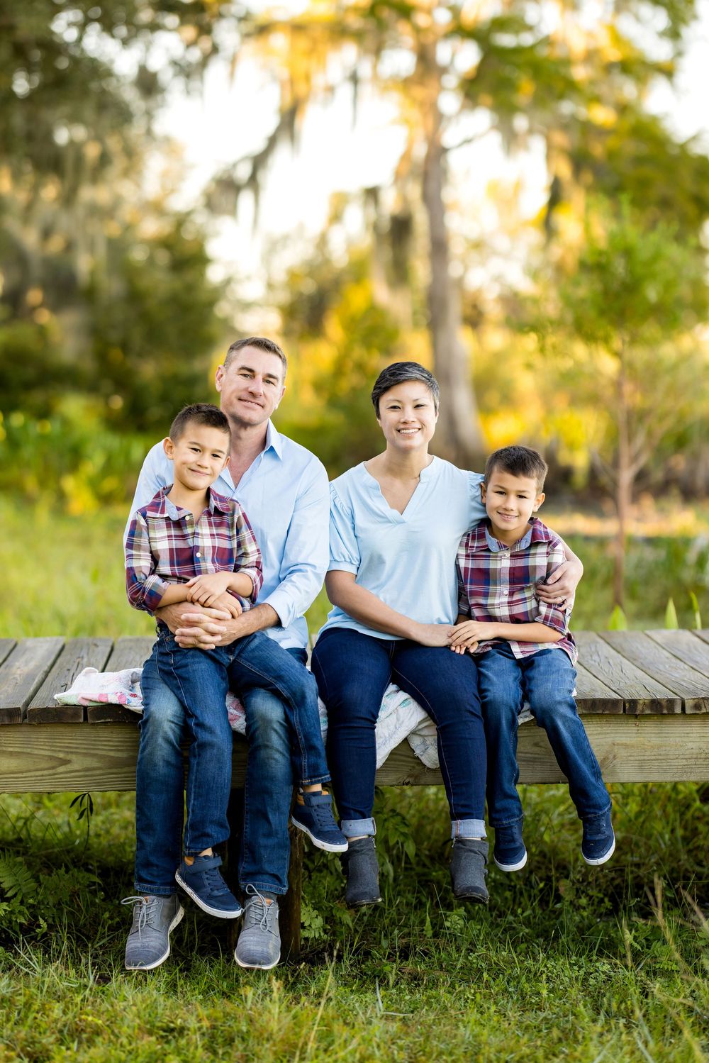 Family members sit together on wooden deck during golden hour sunset in a park setting.