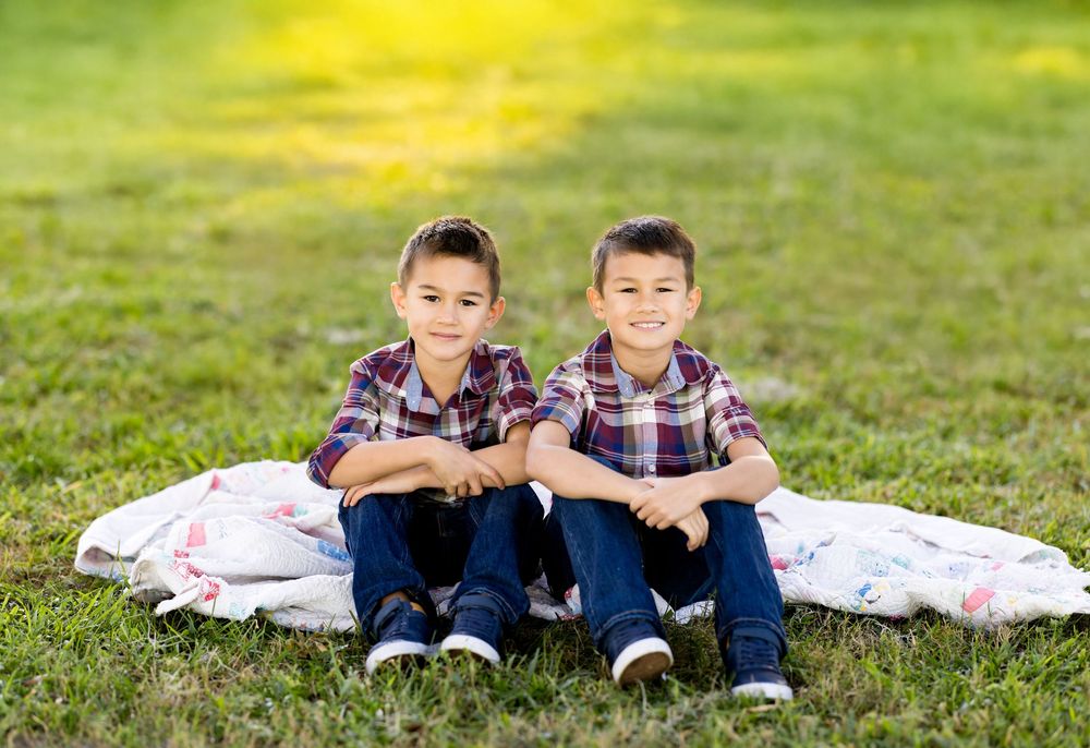 A panoramic series of photos showing two children sitting together on a blanket in green grass on a sunny day.
