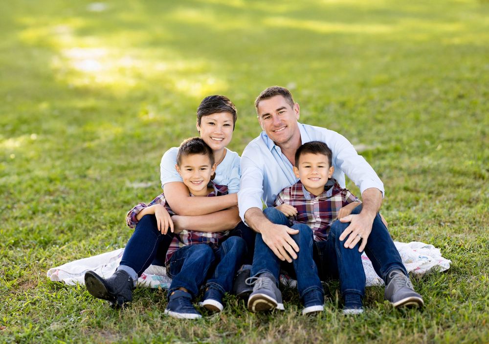 Family members in coordinating blue and white outfits relax together on green grass during outdoor photo session.